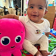 Maeviel is registered to the contest to win money with this photo: baby, child, plush_toy, octopus, pink, mickey_mouse, white_shirt, colorful_bed, indoor, smiling, happy, cute, sitting, toy, soft, cozy, person, face, footwear, clothing
