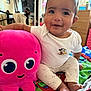 baby, child, plush_toy, octopus, pink, mickey_mouse, white_shirt, colorful_bed, indoor, smiling, happy, cute, sitting, toy, soft, cozy, person, face, footwear, clothing