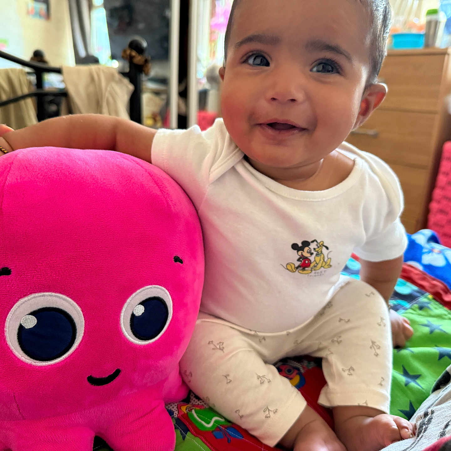 Maeviel is registered to the contest to win money with this photo: baby, child, clothing, colorful_bed, cozy, cute, face, footwear, happy, indoor, mickey_mouse, octopus, person, pink, plush_toy, sitting, smiling, soft, toy, white_shirt