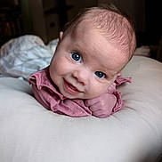 Eliza is registered to the contest to win money with this photo: baby, infant, blue_eyes, smile, tummy_time, pillow, pink_clothes, portrait, indoors, soft_lighting, close_up, cute, skin, hand, blanket, bedroom, nursery, gaze, head, expression