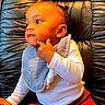 baby, child, infant, sitting, red_pants, white_top, black_chair, leather_chair, curious_expression, pointing, indoors, portrait, young_child, cute, face, person, small_child, babys_bib, comfortable, thoughtful