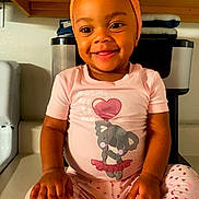 London is registered to the contest to win money with this photo: toddler, child, smiling, pajamas, pink, headband, kitchen, counter, wooden_cabinets, appliance, koala_print, heart_pattern, sitting, indoors, happy, cute, portrait, baby, person, clothing