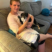 Sissy is registered to the contest to win money with this photo: animal, boy, casual_clothing, companionship, couch, dog, domestic, friendly, human, indoor, living_room, pet, pillow, relaxed, seated, shorts, smile, tshirt, wooden_floor, young_person