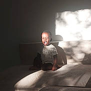 Ousseynou Sy participe au concours pour gagner de l'argent avec cette photo : child, couch, sunlight, shadow, indoor, expression, texture, furniture, person, seated, light, home, casual_clothing, short_hair, smiling, daylight, relaxing, young, happy, portrait