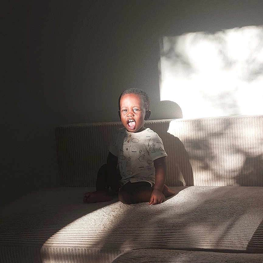 Ousseynou Sy participe au concours pour gagner de l'argent avec cette photo : casual_clothing, child, couch, daylight, expression, furniture, happy, home, indoor, light, person, portrait, relaxing, seated, shadow, short_hair, smiling, sunlight, texture, young