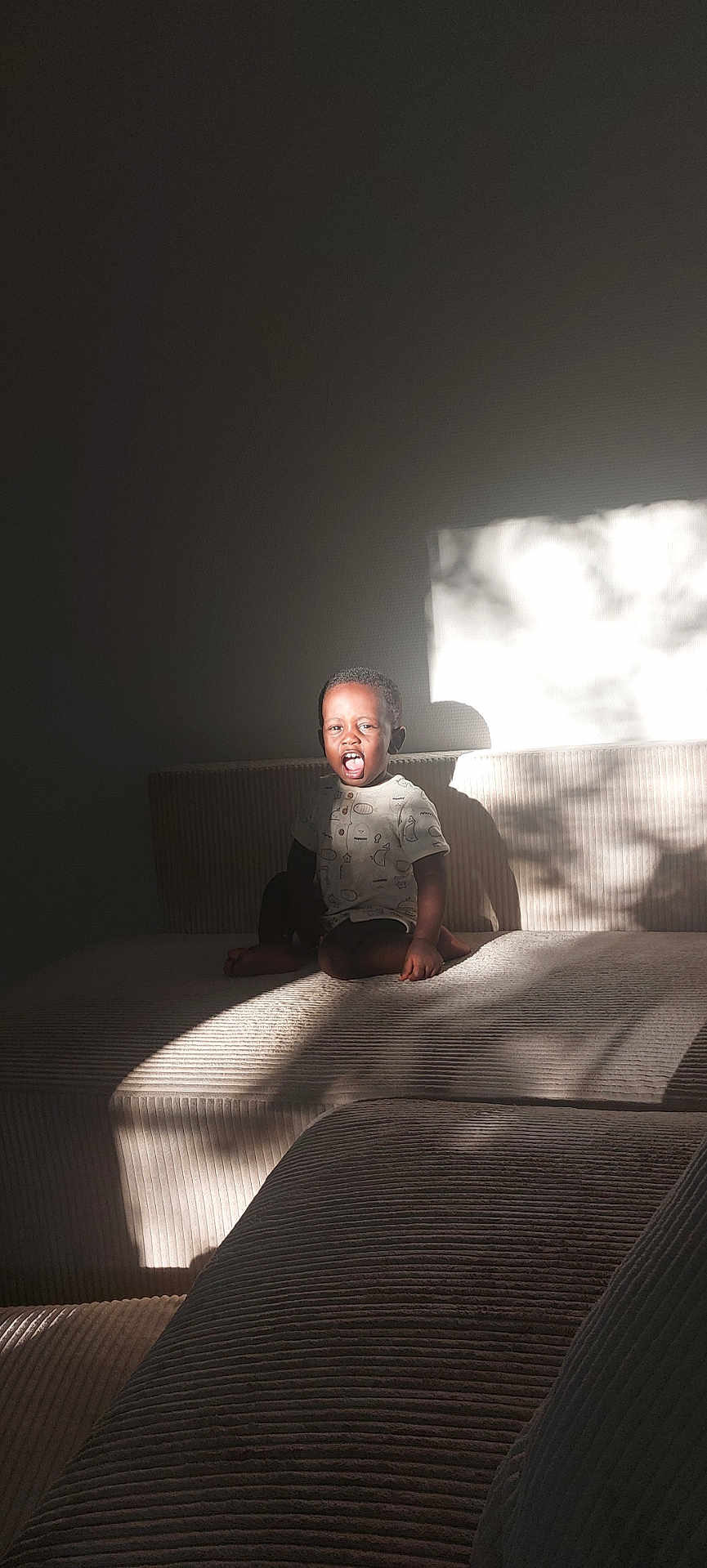 Ousseynou Sy participe au concours pour gagner de l'argent avec cette photo : child, couch, sunlight, shadow, indoor, expression, texture, furniture, person, seated, light, home, casual_clothing, short_hair, smiling, daylight, relaxing, young, happy, portrait
