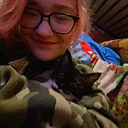 Luna is registered to the contest to win money with this photo: bed, black_and_white_cat, blanket, camouflage, casual, cat, colorful_blanket, cozy, face, feline, glasses, indoor, person, pet, portrait, red_hair, smile, snuggling, soft_fabric, warm