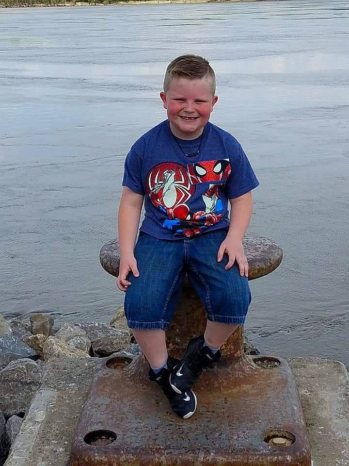 Carson is registered to the contest to win money with this photo: electric_blue, footwear, fun, happy, joy, lake, leg, leisure, person, rock, shorts, sitting, smile, sneakers, soil, t_shirt, thigh, travel, vacation, vertebrate