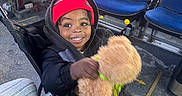 Noah is registered to the contest to win money with this photo: toddler, child, smiling, stroller, teddy_bear, red_beanie, black_jacket, bus, blue_seats, floor_marking, happy, indoor, person, footwear, casual_clothing, seat, window, hand, toy, transportation