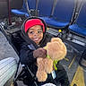 toddler, child, smiling, stroller, teddy_bear, red_beanie, black_jacket, bus, blue_seats, floor_marking, happy, indoor, person, footwear, casual_clothing, seat, window, hand, toy, transportation