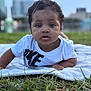 Jayce joined the competition — help win amazing prizes! baby, child, infant, blanket, grass, outdoor, nature, tshirt, face, eyes, mouth, curly_hair, portrait, laying_down, young_child, daylight, urban_background, closeup, expression, person