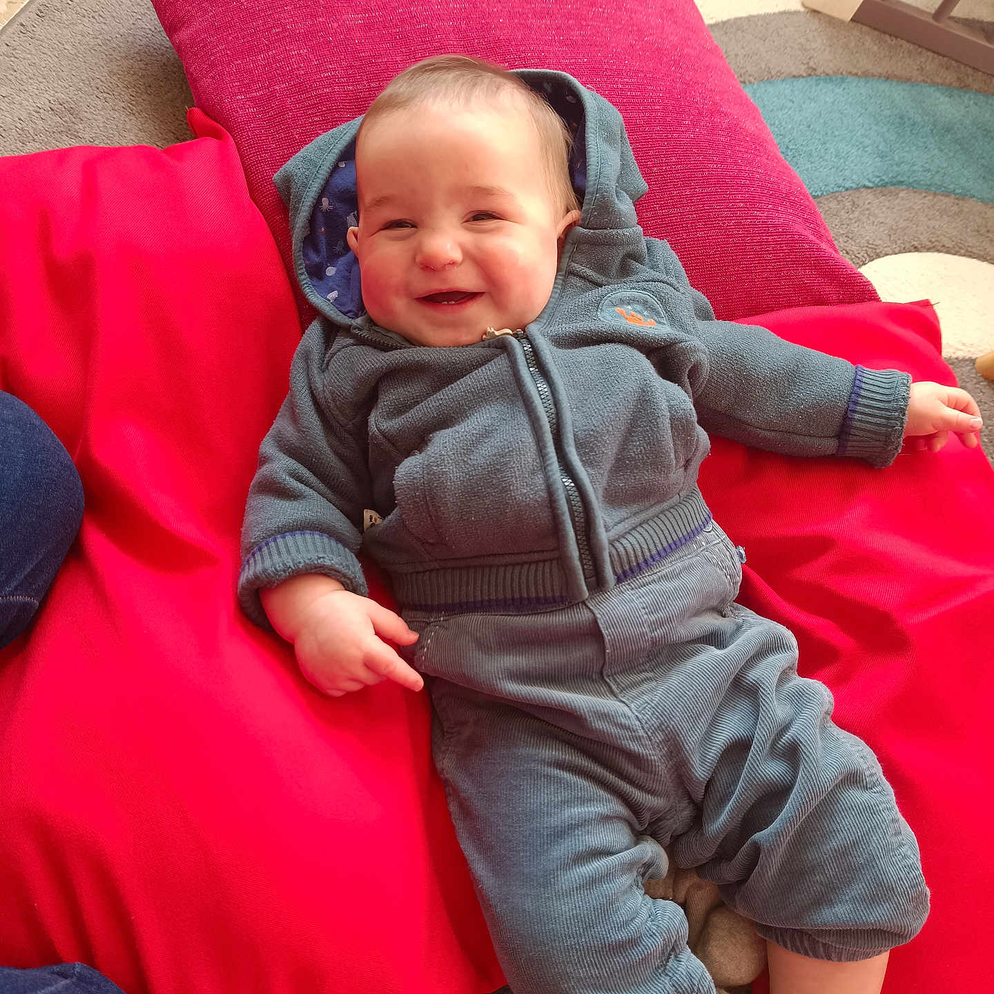 Lucas a rejoint le concours — aidez-le/la à gagner de superbes lots ! baby, blue, carpet, casual_clothing, child, cozy, cushions, cute, floor, happy, home, hoodie, indoor, infant, pants, person, playful, red, relaxing, smiling