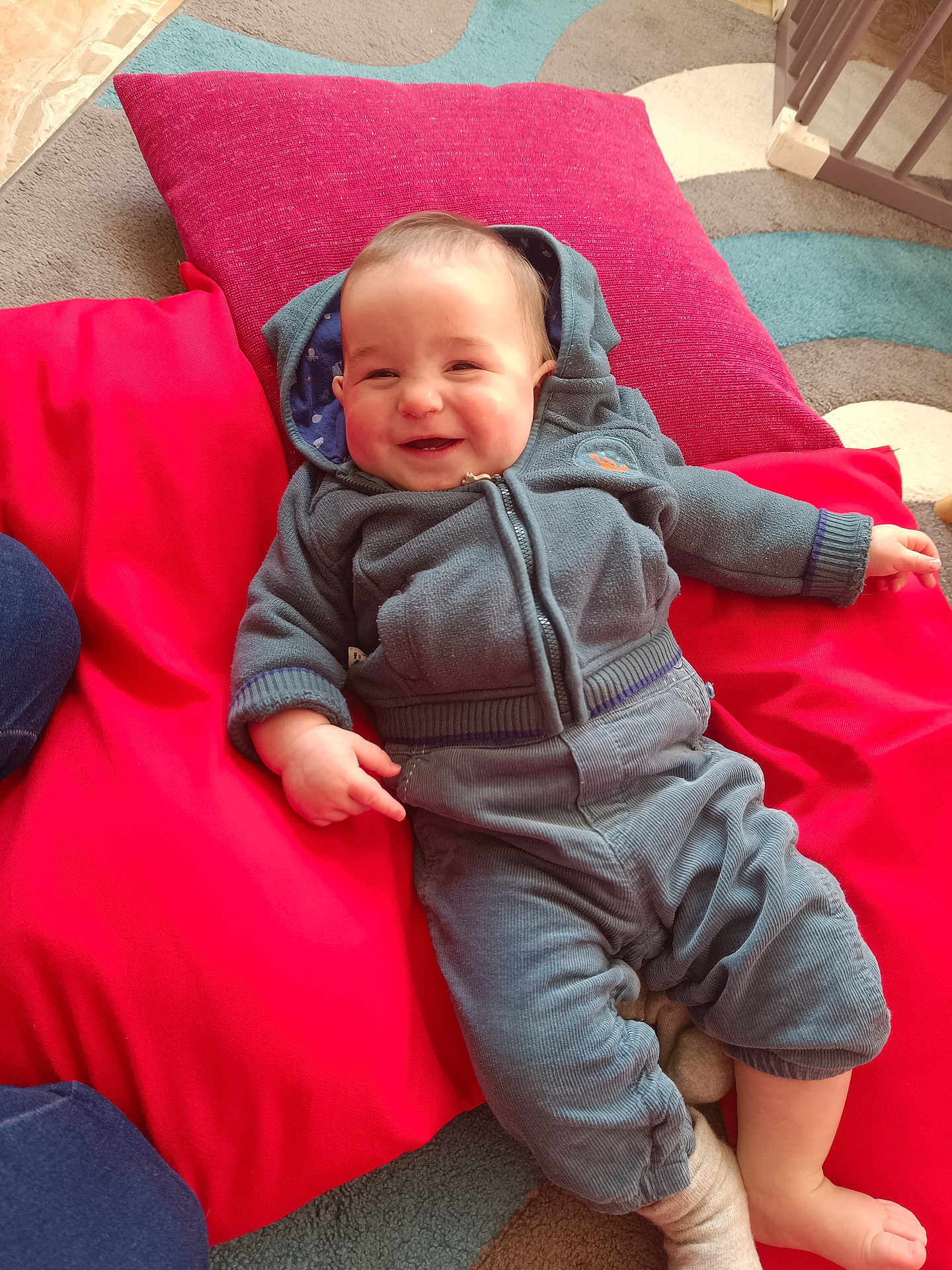 Lucas a rejoint le concours — aidez-le/la à gagner de superbes lots ! baby, child, smiling, hoodie, pants, cushions, red, blue, carpet, indoor, happy, infant, cute, cozy, relaxing, person, casual_clothing, floor, playful, home