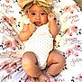 baby, infant, headband, bow, cute, smiling, floral_blanket, pattern, lying_down, fist, skin, clothing, indoors, portrait, child, newborn, soft_texture, pink, white, decorative_text