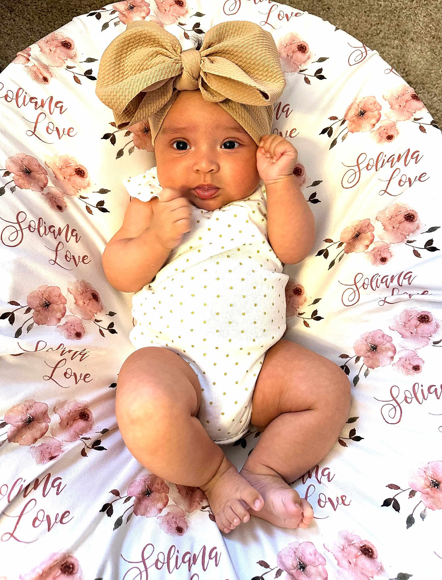 Soliana joined the competition — help win amazing prizes! baby, infant, headband, bow, cute, smiling, floral_blanket, pattern, lying_down, fist, skin, clothing, indoors, portrait, child, newborn, soft_texture, pink, white, decorative_text