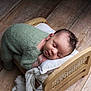 Isaiah participe au concours pour gagner de l'argent avec cette photo : baby, sleeping, knitted_outfit, green_clothing, wooden_bed, pillow, blanket, floor, wood_floor, infant, peaceful, cozy, resting, cute, portrait, indoor, newborn, child, soft_lighting, calm