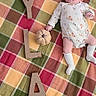 baby, infant, child, lying_down, portrait, plaid_blanket, colorful, wooden_letters, name_spelling, stuffed_toy, flower_toy, headband, romper, socks, smiling, indoors, bed, cozy, baby_photoshoot, soft_lighting