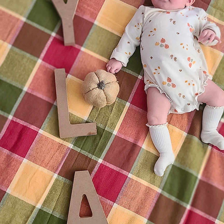 Ayla is registered to the contest to win money with this photo: baby, infant, child, lying_down, portrait, plaid_blanket, colorful, wooden_letters, name_spelling, stuffed_toy, flower_toy, headband, romper, socks, smiling, indoors, bed, cozy, baby_photoshoot, soft_lighting