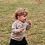 toddler, child, grass, outdoor, field, snack, walking, happy, expression, hand, pointing, shorts, sweater, shoes, pink_socks, nature, daylight, playful, motion, casual_clothing