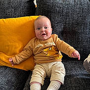 Maël a rejoint le concours — aidez-le/la à gagner de superbes lots ! adult_in_background, baby, blue_eyes, child, couch, cozy, cute, furniture, happy, home_interior, infant, lion_king, living_room, onesie, pillow, portrait, smile, socks, sofa, yellow_pillow
