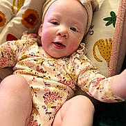 Asha is registered to the contest to win money with this photo: baby, infant, headband, floral_clothing, cushion, pattern, animal_print, smiling, closeup, face, skin, arm, legs, indoors, cute, child, happy, soft_toys, comfort, playful