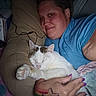 cat, person, sleeping, cuddling, pet, white_cat, tabby, animal, face, smiling, indoors, bed, pillow, blanket, blue_shirt, hand, purple_nails, tattoo, cozy, portrait