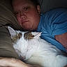 cat, person, sleeping, pet, bed, bedroom, snuggling, white_cat, tabby_cat, fur, whiskers, ears, closed_eyes, portrait, indoor, resting, cuddling, blue_shirt, pillow, cozy