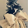 cat, tuxedo_cat, christmas_tree, holiday, tree, decoration, burlap_bow, ribbon, frosted_branches, indoor, portrait, black_and_white, pet, feline, sitting, peeking, greenery, festive, home_decor, funny