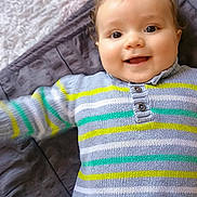 Wassim participe au concours pour gagner de l'argent avec cette photo : baby, child, smile, sweater, striped_clothing, pants, bed, blanket, happy, face, infant, cute, lying_down, person, indoors, young_child, clothing, portrait, head, playful