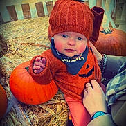 Remi joined the competition — help win amazing prizes! baby, child, pumpkin, hay, orange_clothing, knit_hat, halloween, bib, autumn, seasonal, cute, hand, person, outdoor, smiling, face, festive, holiday, warm_clothing, young_child
