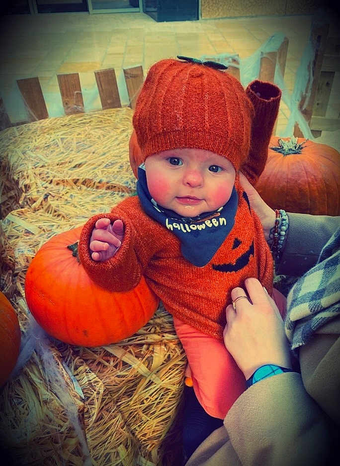 Remi joined the competition — help win amazing prizes! baby, child, pumpkin, hay, orange_clothing, knit_hat, halloween, bib, autumn, seasonal, cute, hand, person, outdoor, smiling, face, festive, holiday, warm_clothing, young_child