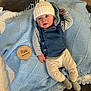Everett is registered to the contest to win money with this photo: baby, infant, child, blue_blanket, knitted_blanket, wooden_plaque, five_months, hat, white_hat, striped_shirt, vest, pants, smiling_face, lying_down, indoor, cozy, cute, soft_toys, warm_clothing, portrait