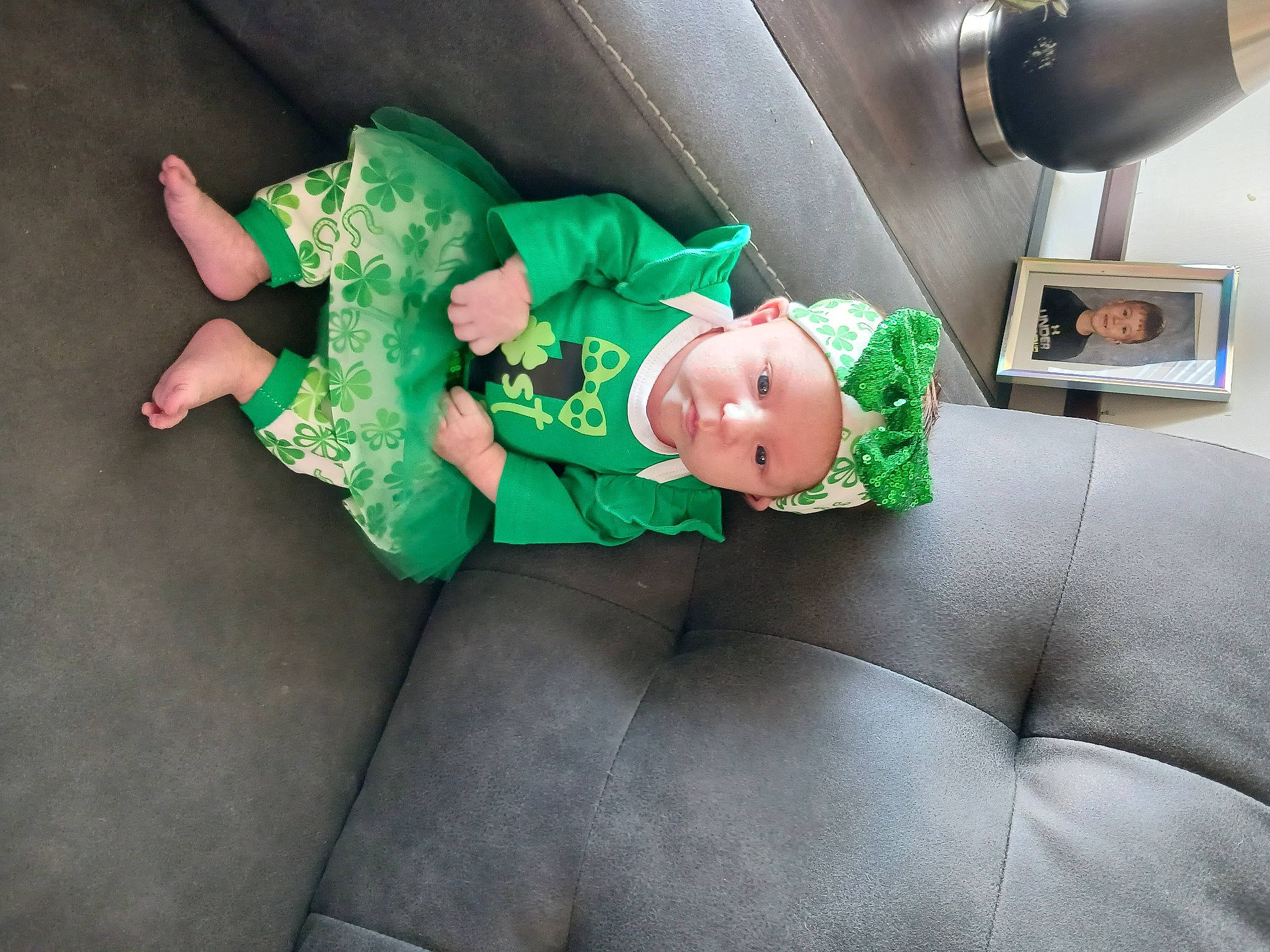 Arianna is registered to the contest to win money with this photo: audio_equipment, baby_toddler_clothing, camera, child, comfort, costume, couch, fictional_character, fun, green, headwear, holiday, lap, machine, mechanical_fan, person, room, sitting, sock, toddler