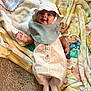 Josiah is registered to the contest to win money with this photo: baby, infant, smiling, hat, romper, blanket, carpet, floor, clothing, cute, child, happy, indoors, soft_texture, toddler, playtime, portrait, baby_bib, feet, laying_down