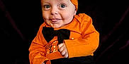 Leo is registered to the contest to win money with this photo: baby, child, halloween, costume, orange_clothing, hat, striped_hat, pumpkin_faces, black_background, cute, tongue_out, smiling, infant, playful, portrait, sitting, black_pants, bow_tie, holiday, festive