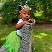J'Liyah is registered to the contest to win money with this photo: toddler, child, girl, green_tutu, crown, outdoor, garden, chair, curious, portrait, cute, fashion, headwear, nature, grass, daylight, person, smile, playful, young_child