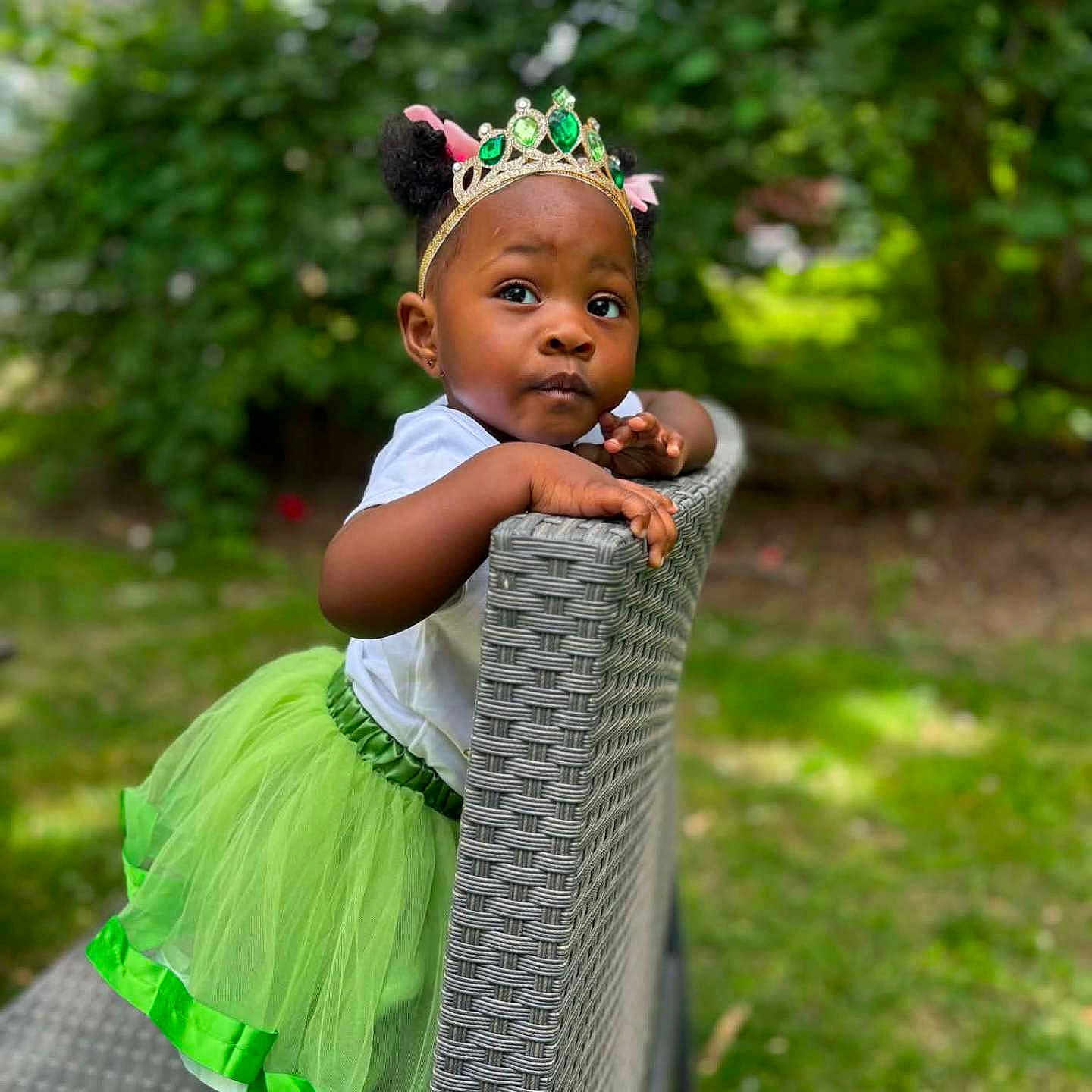 J'Liyah is registered to the contest to win money with this photo: toddler, child, girl, green_tutu, crown, outdoor, garden, chair, curious, portrait, cute, fashion, headwear, nature, grass, daylight, person, smile, playful, young_child