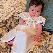 Clara joined the competition — help win amazing prizes! baby, infant, child, white_gown, lace, ribbons, blue_eyes, dark_hair, couch, floral_pattern, pillow, crochet_blanket, vintage_style, indoors, portrait, soft_lighting, relaxed, hand, foot, cute