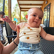 Emma participe au concours pour gagner de l'argent avec cette photo : baby, background, casual_clothing, chair, child, daylight, dimple, expression, face, furniture, hand, outdoor, patio, person, relaxed, shorts, smile, table, tank_top, wooden_beam