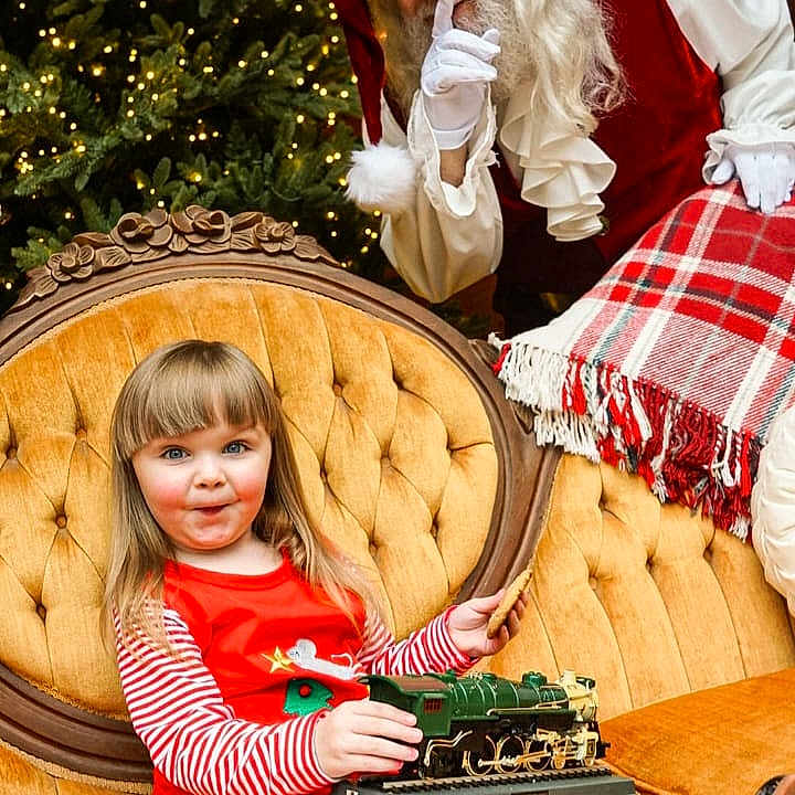 Ruby is registered to the contest to win money with this photo: accessories, adult, child, christmas, christmasdecorations, christmastree, clothing, couch, face, female, festival, furniture, girl, glasses, glove, hat, head, person, santaclaus, woman