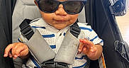 Messiah is registered to the contest to win money with this photo: baby, child, sunglasses, stroller, curly_hair, seatbelt, striped_shirt, cute, hands, feet, blanket, infant, smile, wearing, sitting, indoors, person, young, casual, fashion