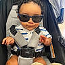 baby, child, sunglasses, stroller, curly_hair, seatbelt, striped_shirt, cute, hands, feet, blanket, infant, smile, wearing, sitting, indoors, person, young, casual, fashion