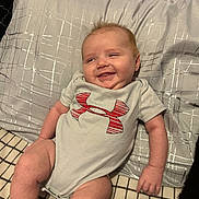 Jaxon joined the competition — help win amazing prizes! baby, smiling, infant, onesie, pillow, blanket, indoor, person, cute, happy, child, clothing, pattern, fabric, head, face, skin, arm, leg, relaxing