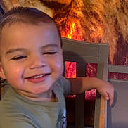 Nathaniel joined the competition — help win amazing prizes! background, brown, casual_clothing, chair, child, face, glow, happy, home, indoor, lion_image, orange, person, red, short_hair, smiling, toddler, warm_lighting, wooden_chair, young_child