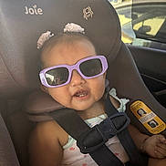 Arabella is registered to the contest to win money with this photo: baby, child, car_seat, sunglasses, hair_bows, seatbelt, smile, indoors, infant, cute, safety, clothing, accessory, portrait, seat, car, young_child, happiness, fashion, person