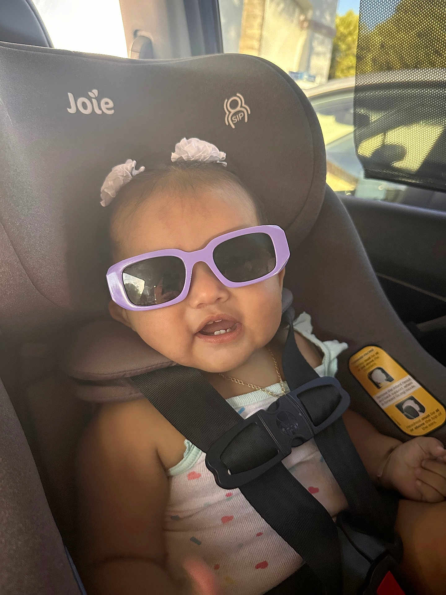 Arabella is registered to the contest to win money with this photo: baby, child, car_seat, sunglasses, hair_bows, seatbelt, smile, indoors, infant, cute, safety, clothing, accessory, portrait, seat, car, young_child, happiness, fashion, person
