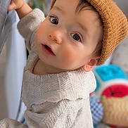 Merlin a rejoint le concours — aidez-le/la à gagner de superbes lots ! baby, child, hat, knit_hat, sweater, cream_sweater, curious, indoors, face, person, infant, hand, railing, soft_light, closeup, portrait, cute, warm_clothing, background_blur, toy