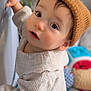 baby, child, hat, knit_hat, sweater, cream_sweater, curious, indoors, face, person, infant, hand, railing, soft_light, closeup, portrait, cute, warm_clothing, background_blur, toy