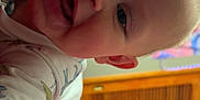 Maverick joined the competition — help win amazing prizes! baby, infant, smiling, closeup, indoor, onesie, blanket, red_bedspread, wooden_cabinet, curtains, face, head, skin, child, person, happy, lying_down, expression, blue_eyes, cozy