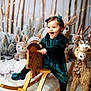baby, child, toddler, rocking_horse, reindeer, stuffed_animal, plush_toy, velvet_dress, hair_bow, smile, holiday_scene, winter_backdrop, fairy_lights, fur_rug, wooden_toy, portrait, studio_photo, decorative_trees, cozy, cute